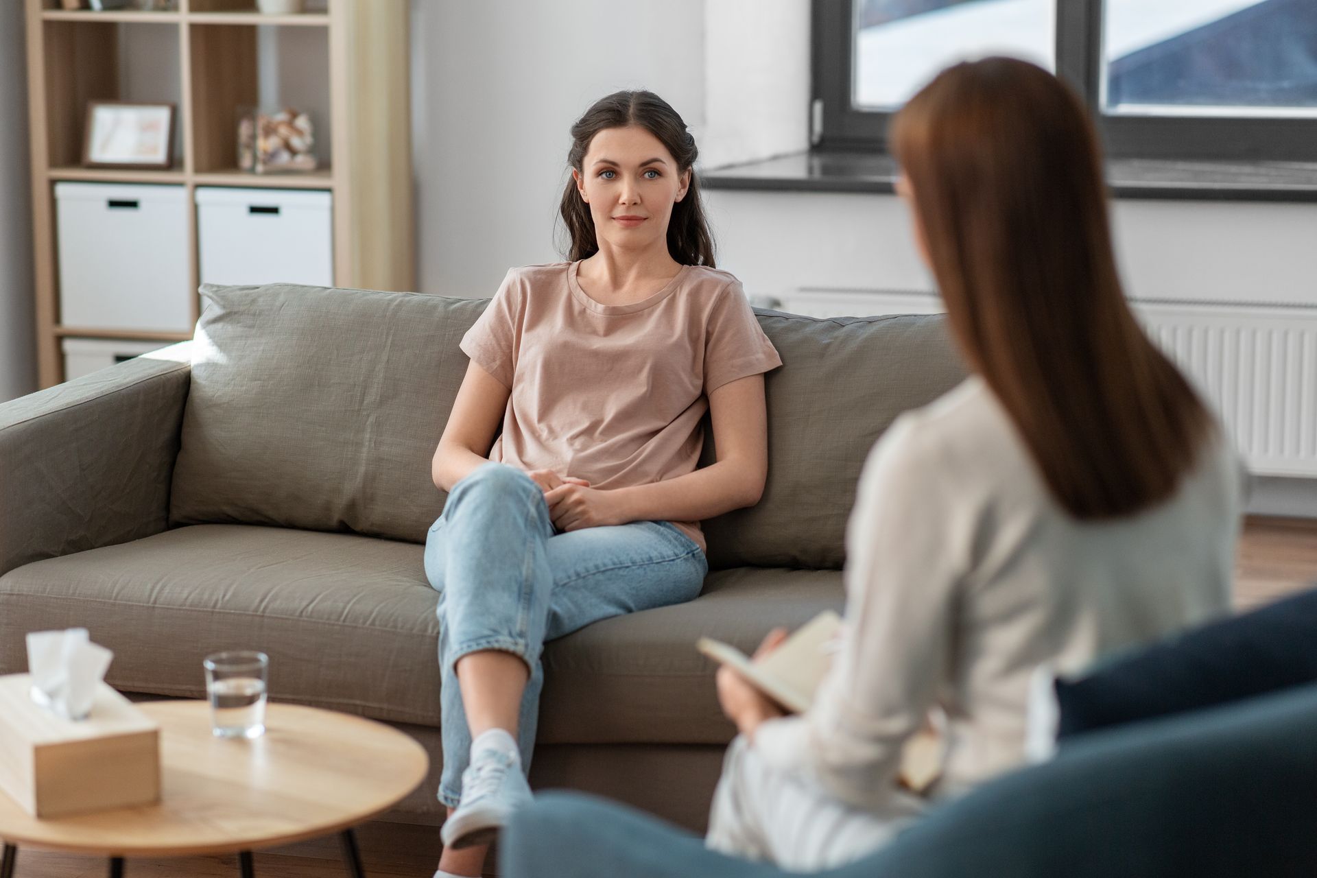 Woman in session with therapist on sofa. Neutral expressions in a living room setting.