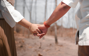 Two people in white shirts holding hands outdoors in a dusty field