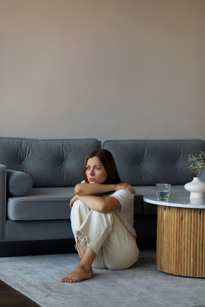 Person sitting on a rug beside a gray sofa and round wooden table in a minimalist living room