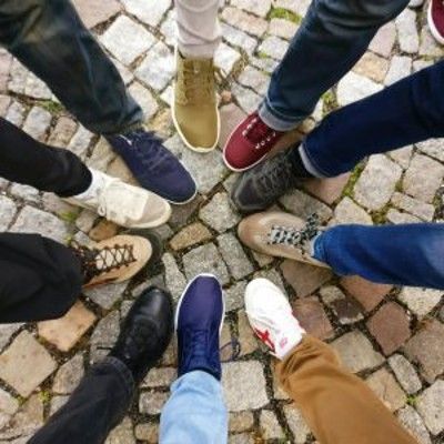 Several pairs of shoes and jeans arranged in a circle on cobblestones