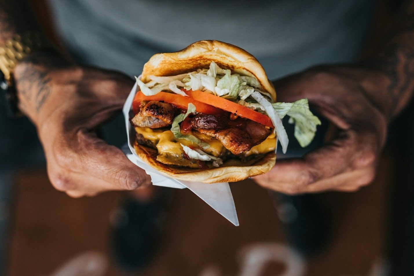 Hands holding a burger with lettuce, tomato, and cheese against a dark background