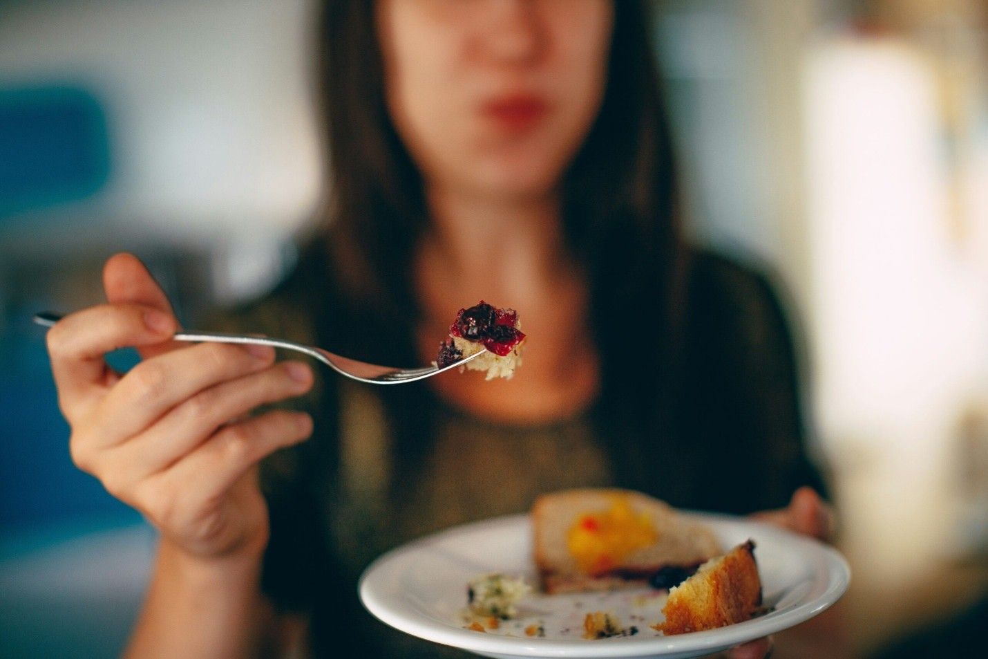 Person holding a spoonful of food over a plate in a softly lit dining setting