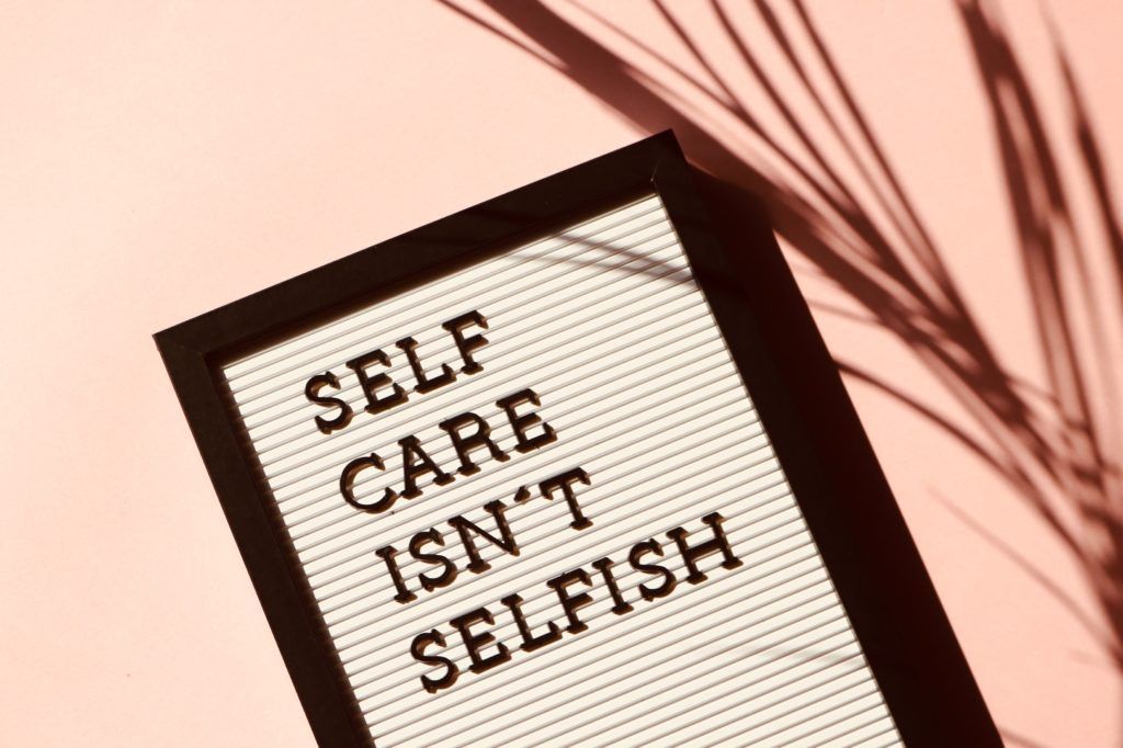 A letter board on a peach background reads, SELF CARE ISN'T SELFISH, next to the shadow of a palm leaf.