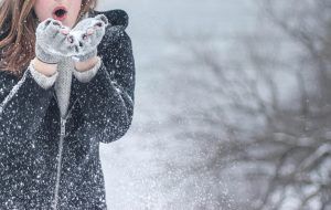 Woman blowing snow from gloved hands, snowy outdoor scene.