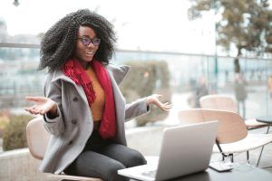 Woman with laptop, gesturing in surprise, wearing coat and scarf outdoors.