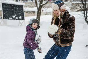 Woman and child in snow, preparing for snowball fight. Both wear winter hats, gloves, and coats.