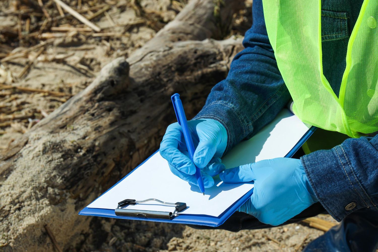 A person wearing blue gloves is writing on a clipboard.