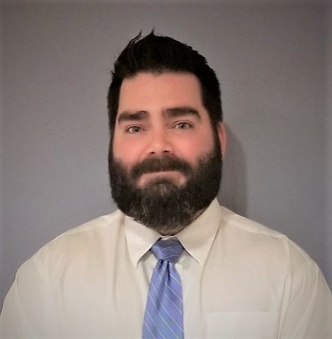 A man with a beard is wearing a white shirt and blue tie.