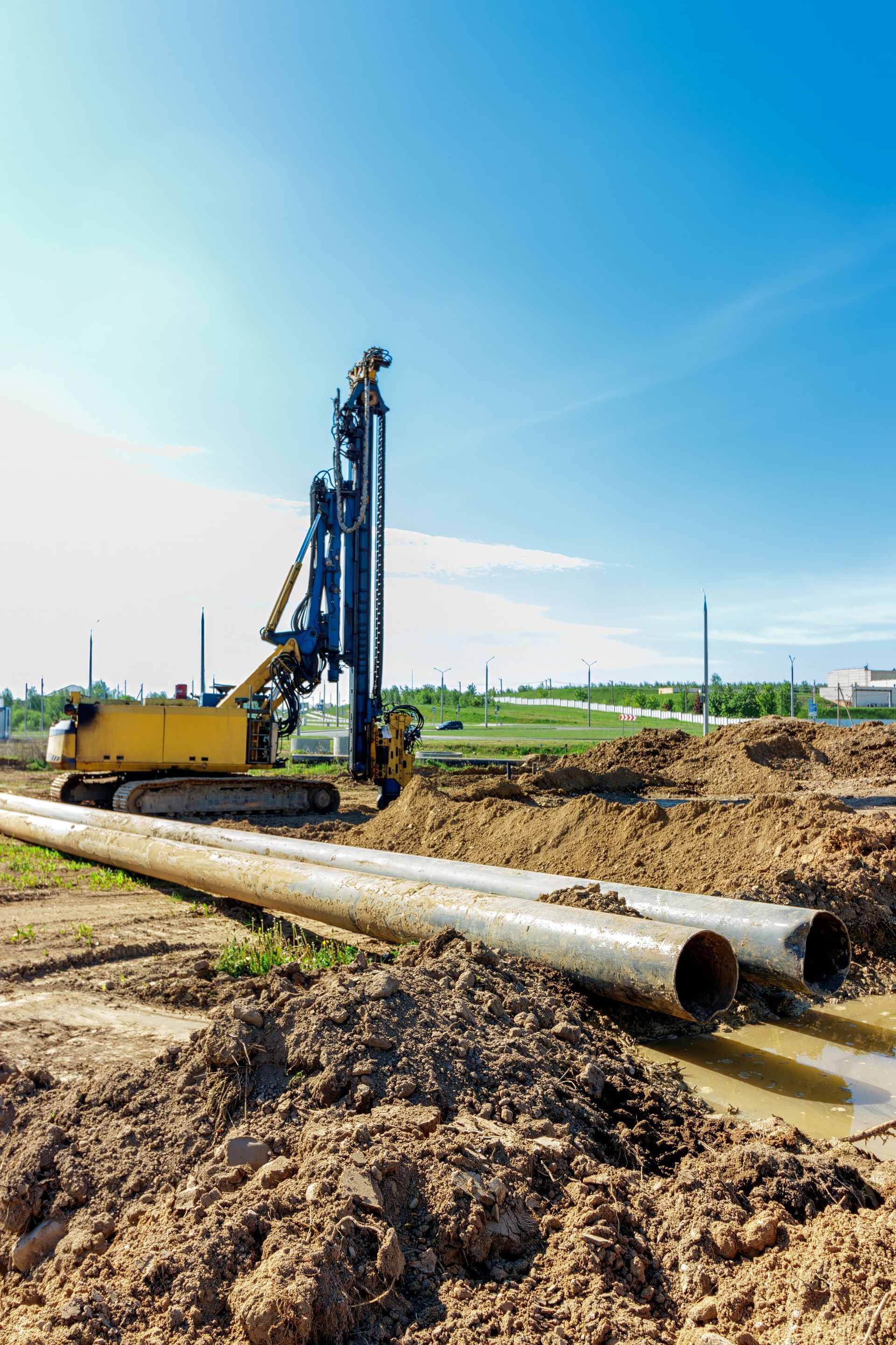 A construction site with a drill and pipes in the dirt.