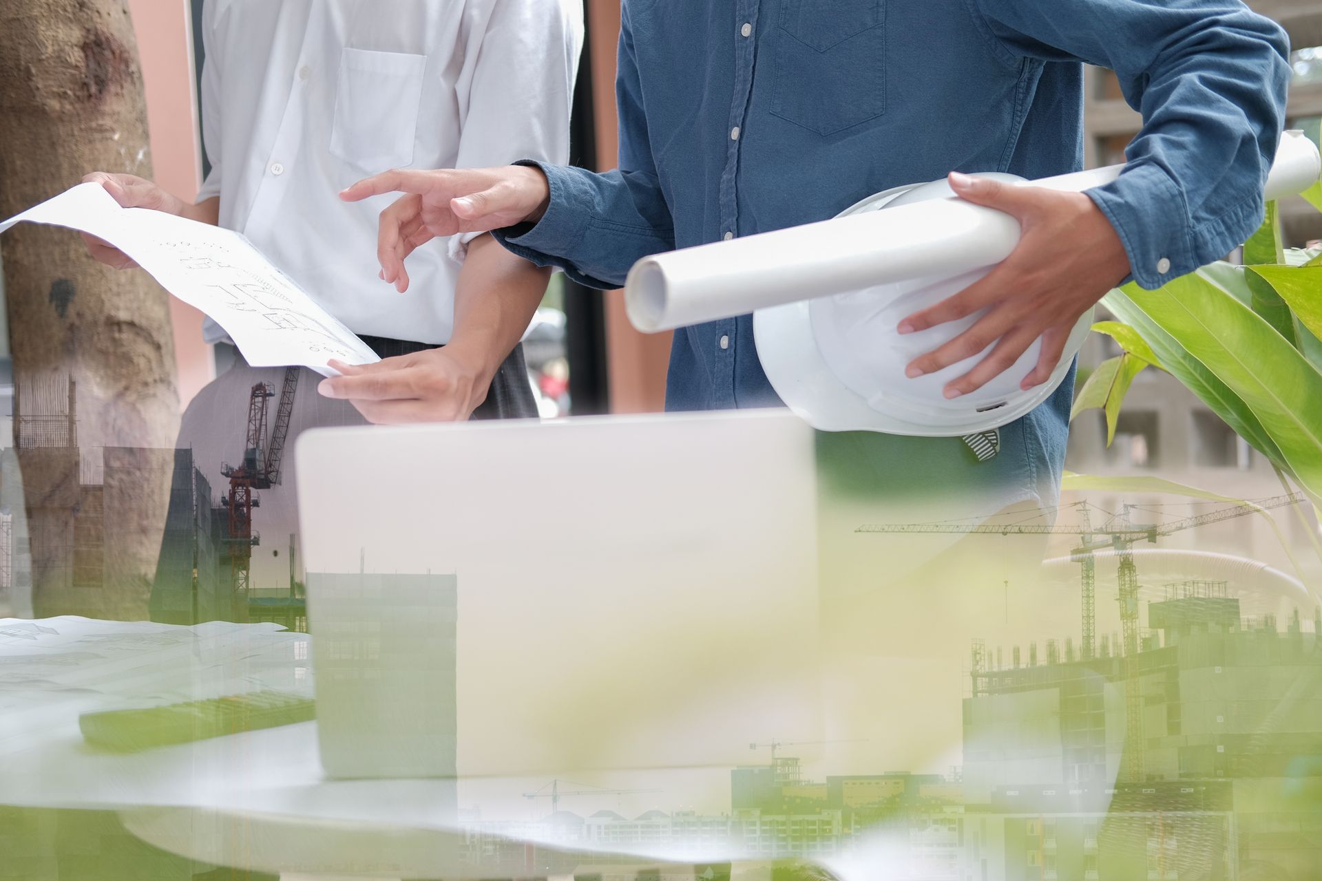 Two men are looking at a laptop and a blueprint.