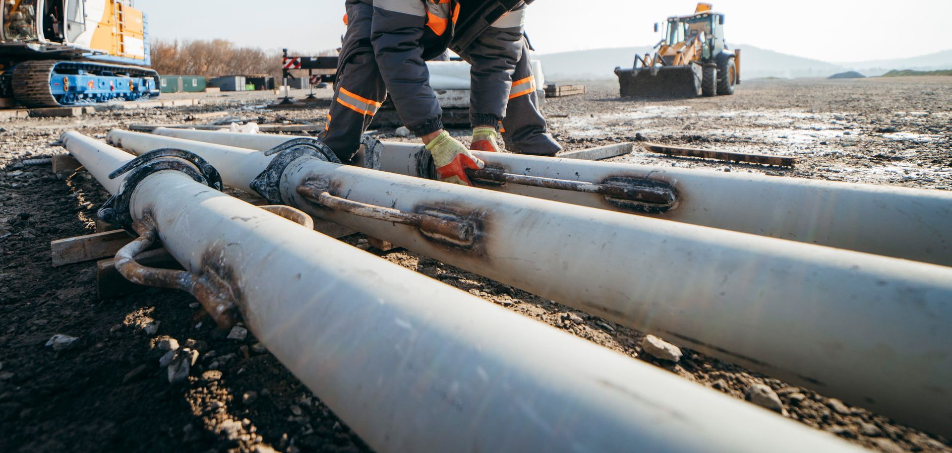 A man is standing on a pile of pipes on a construction site.