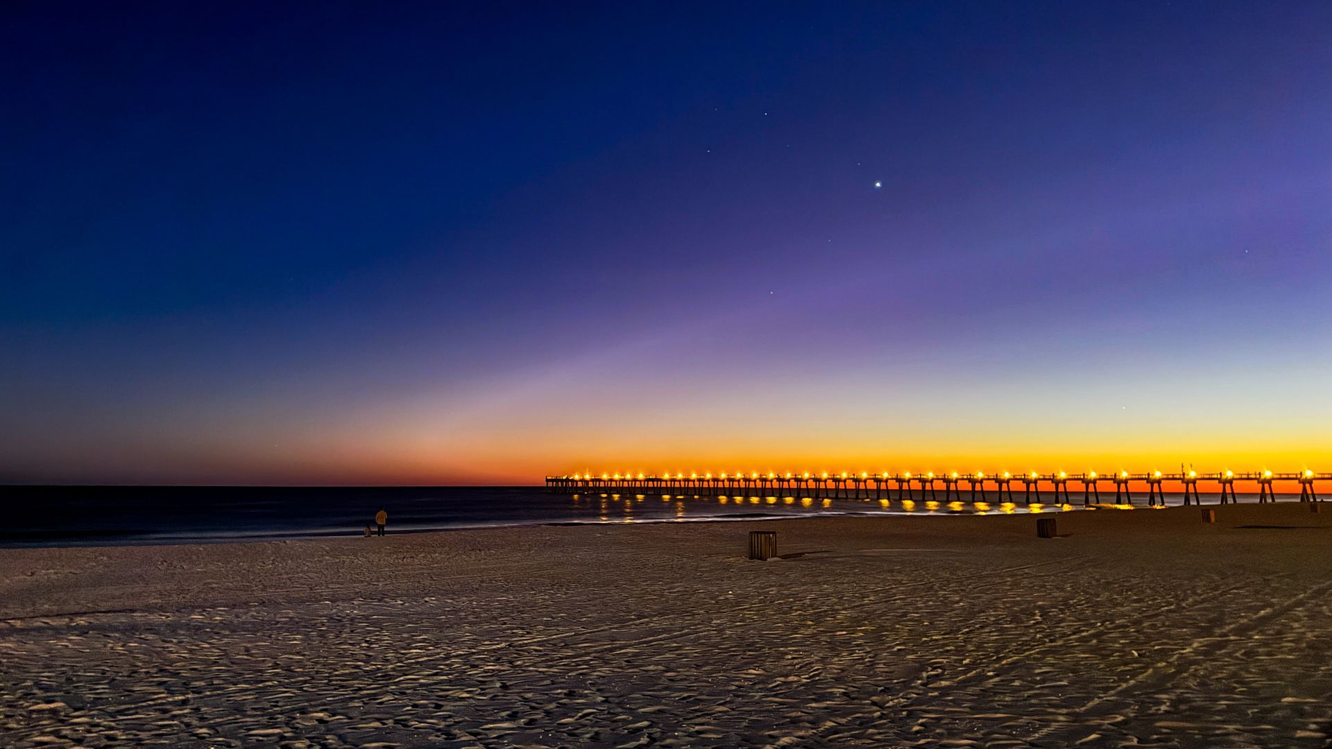 A pier is lit up at sunset on a beach.