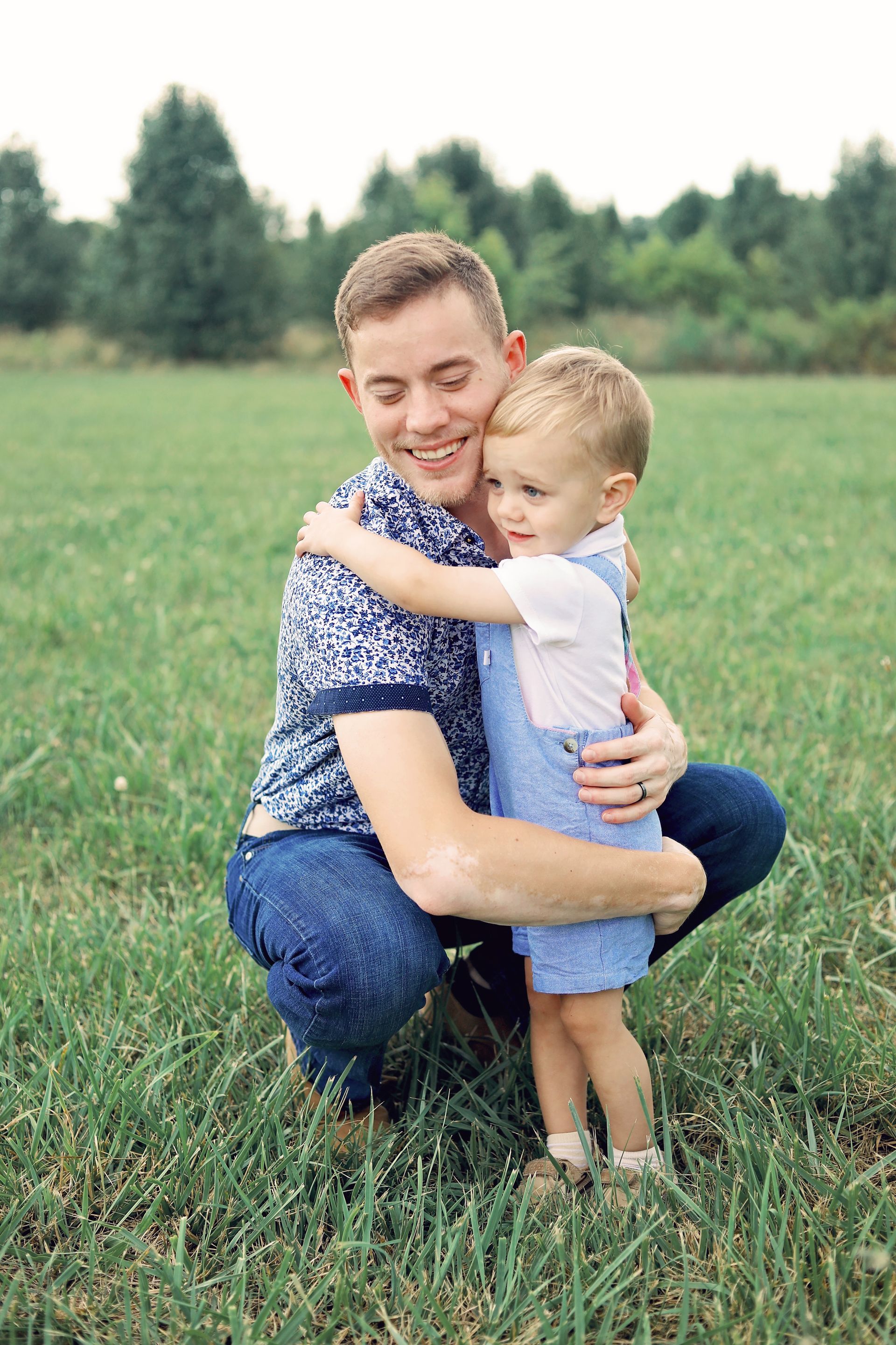 A man is kneeling down and hugging a little boy in a field.