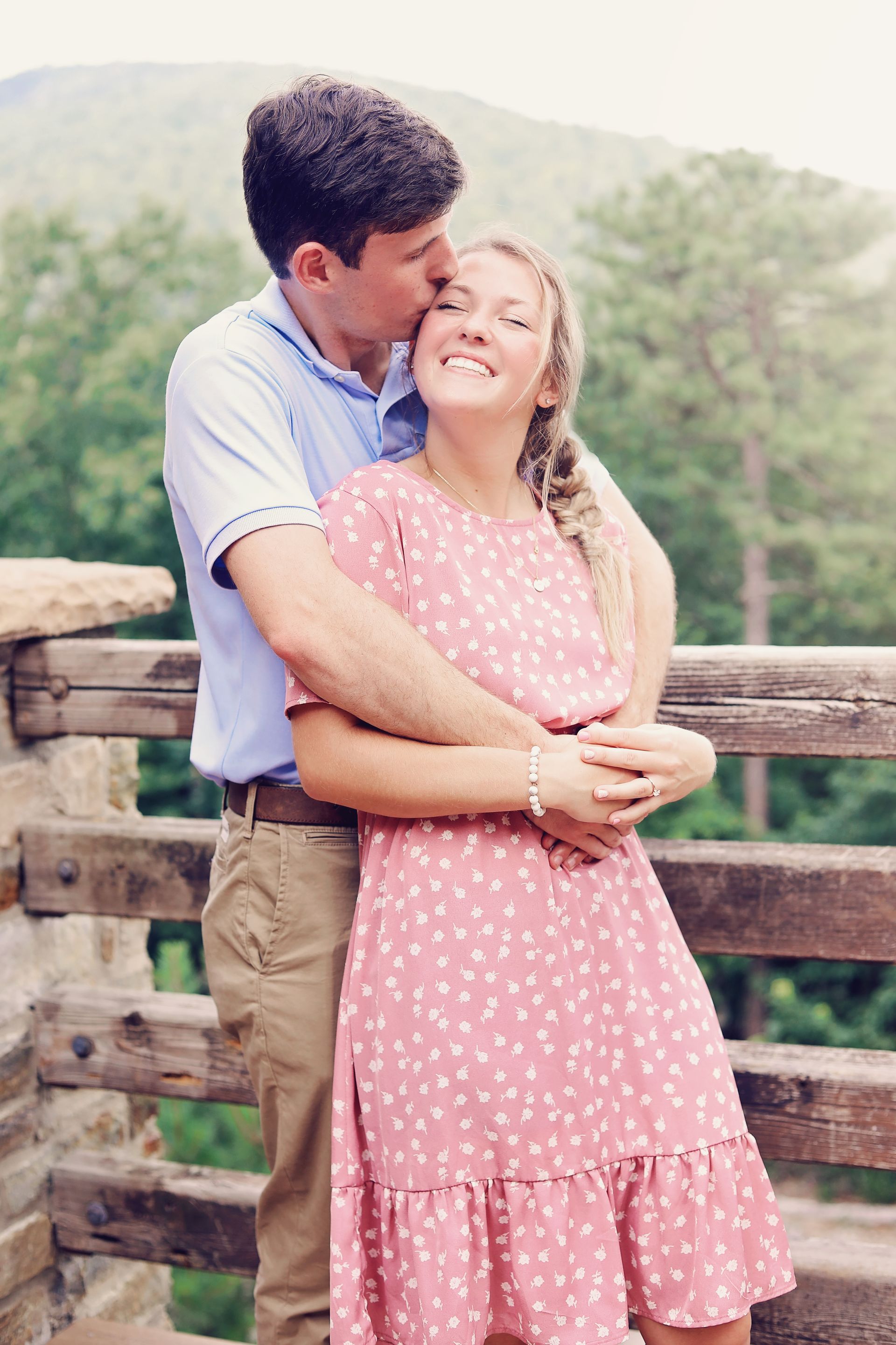 A man is kissing a woman on the cheek while standing next to a wooden fence.
