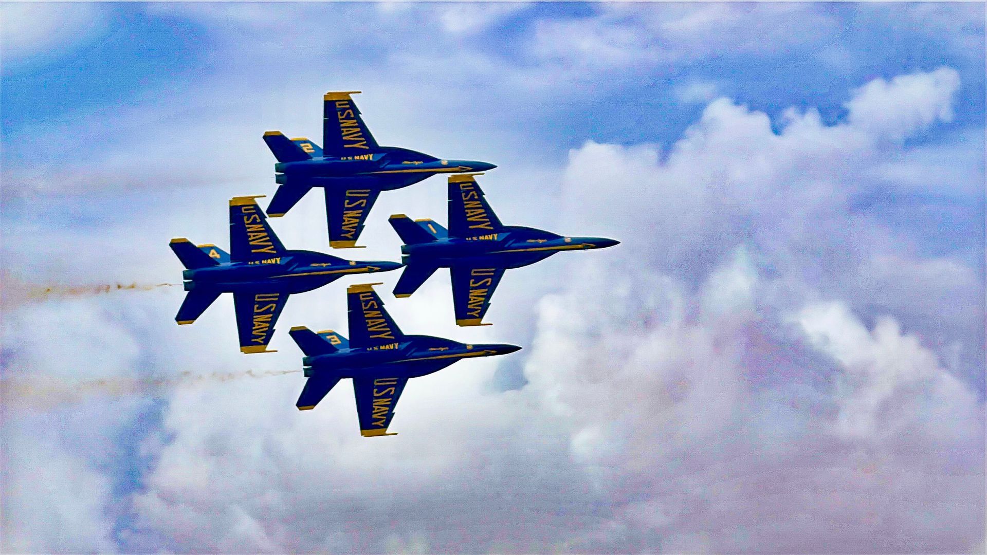 Four blue and yellow jets are flying in formation in the sky.