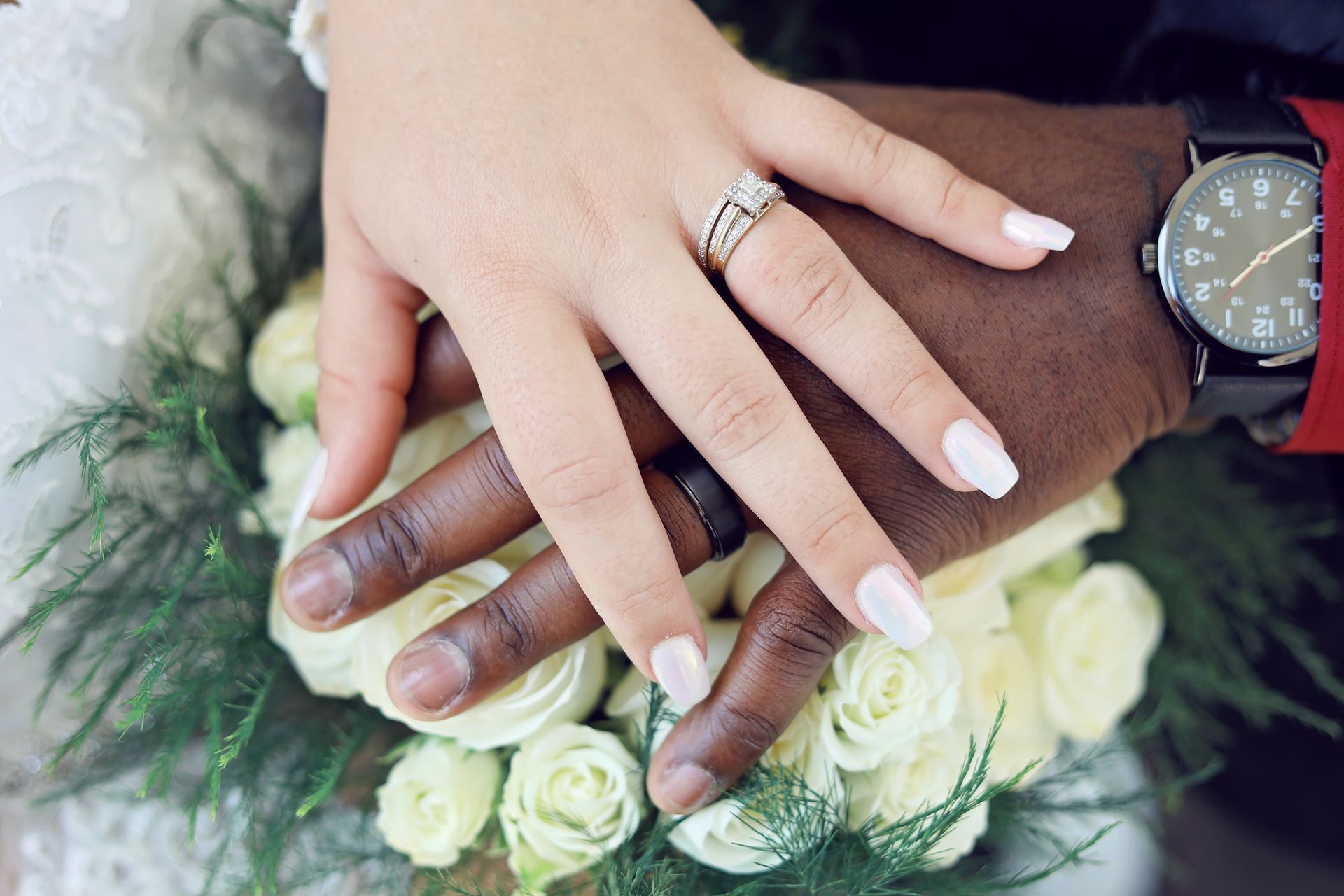 A close up of a bride and groom 's hands with wedding rings holding a bouquet of flowers.