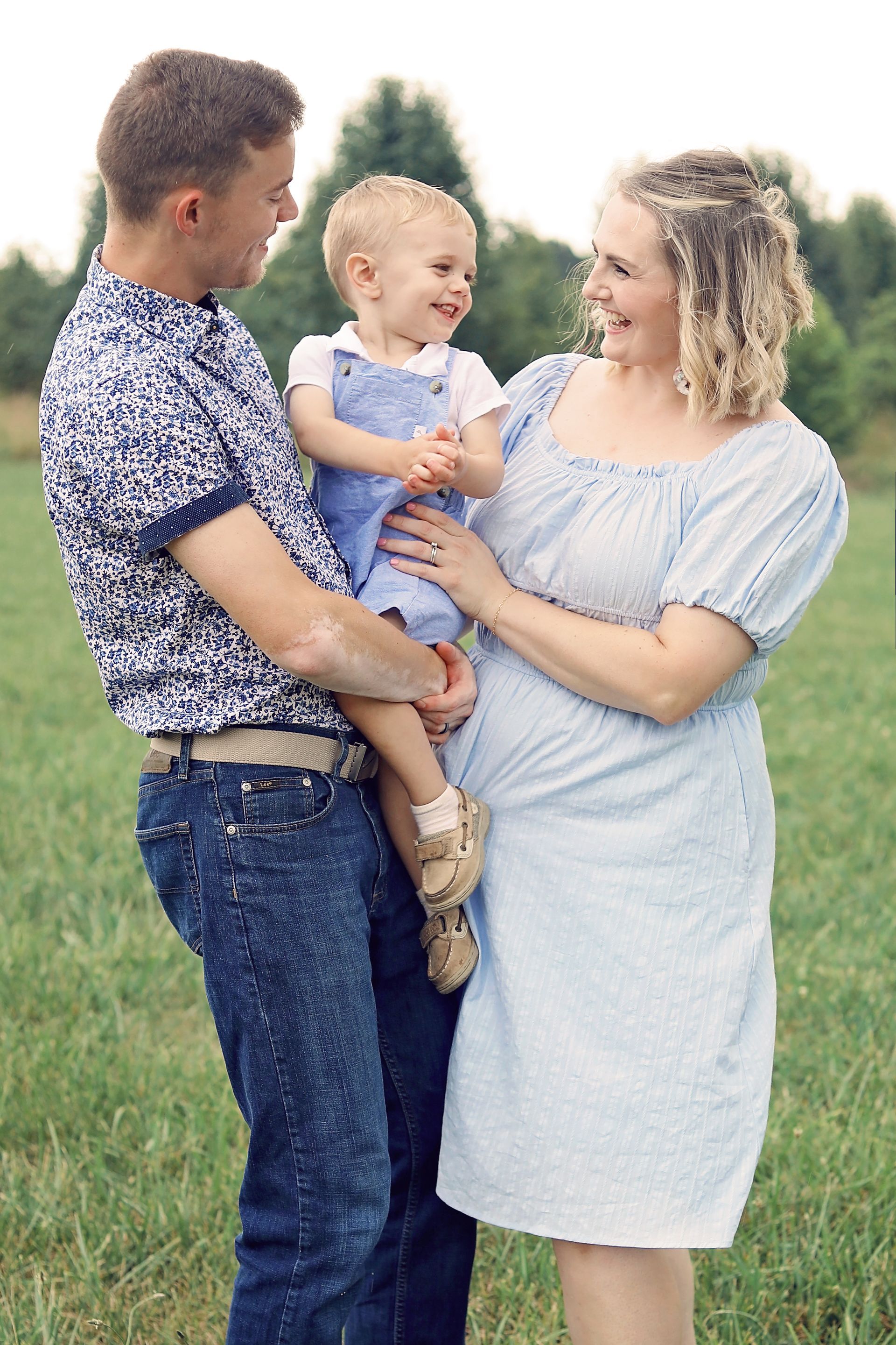A man and a woman are holding a baby in a field.