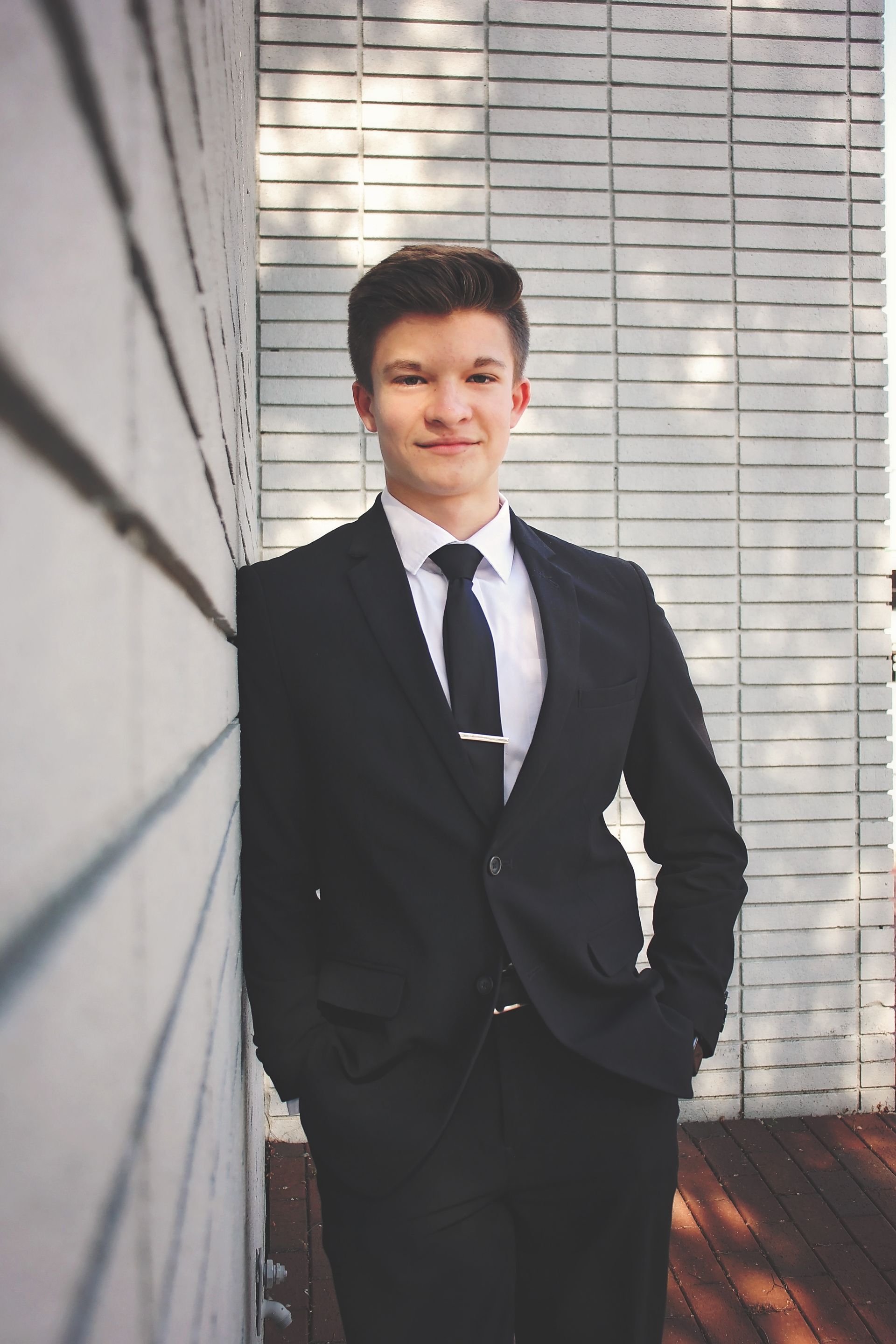 A young man in a suit and tie is leaning against a wall.