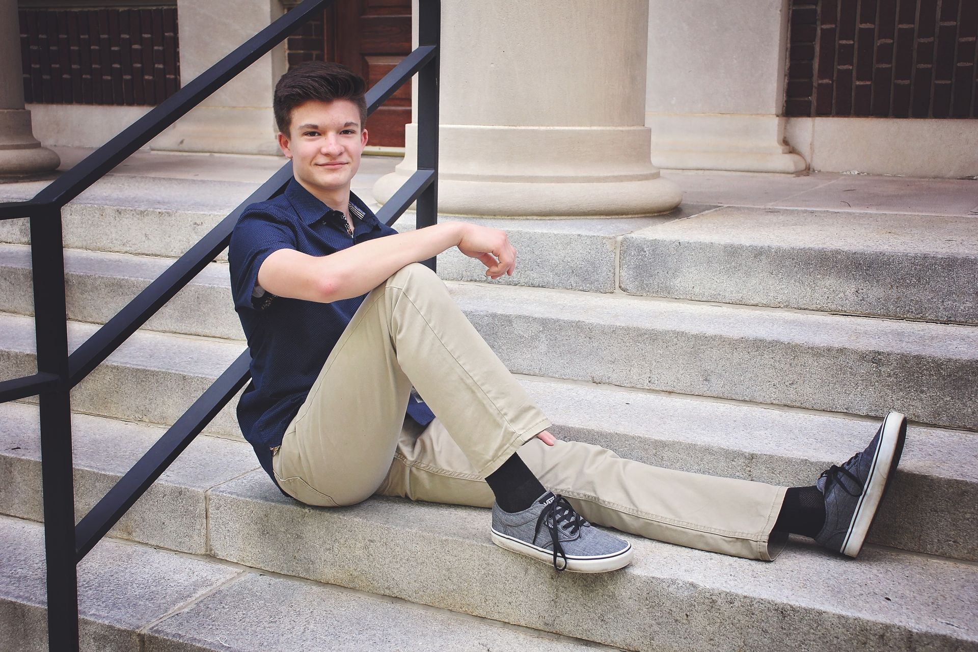 A young man is sitting on the steps of a building.
