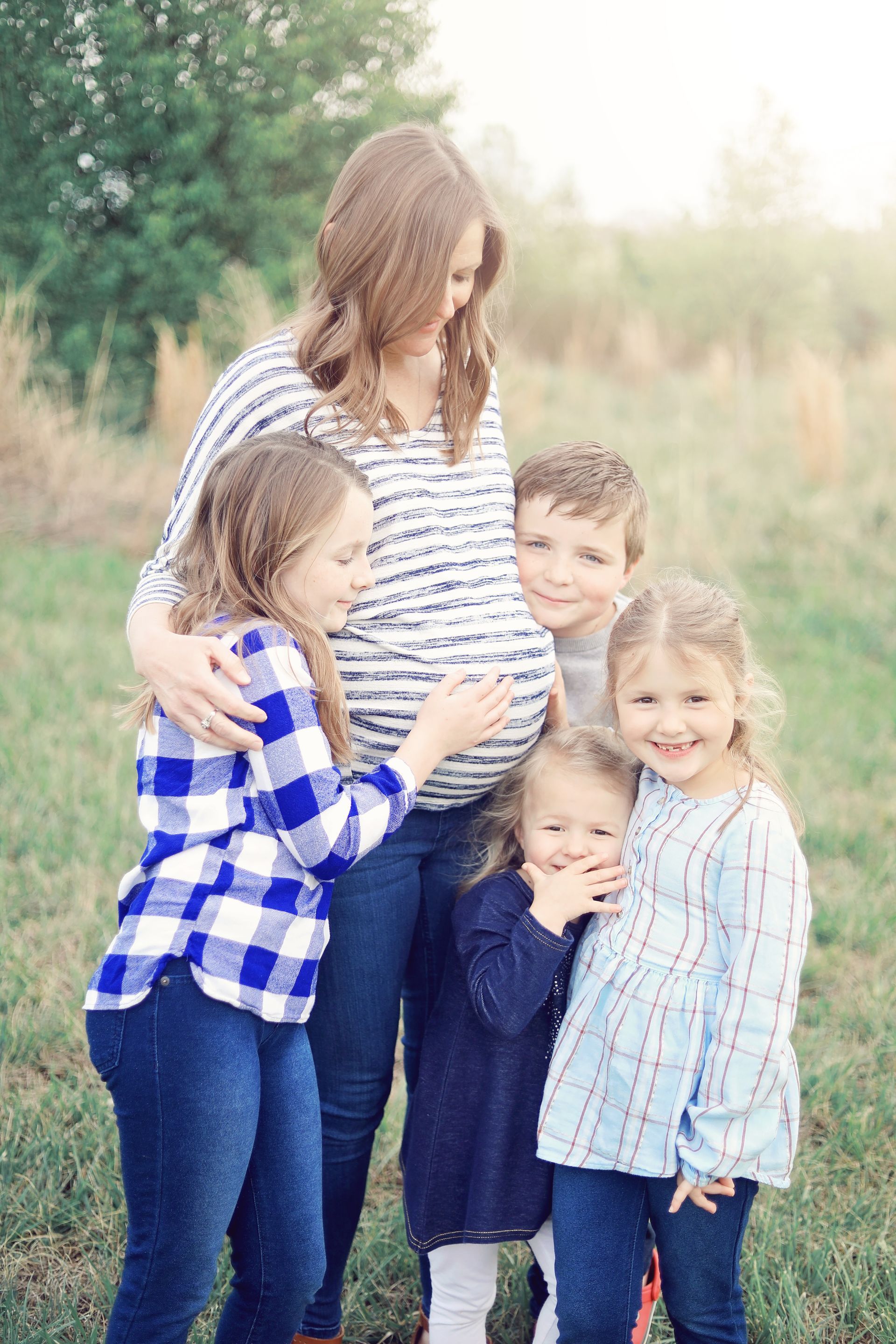 A pregnant woman is standing in a field with three children.