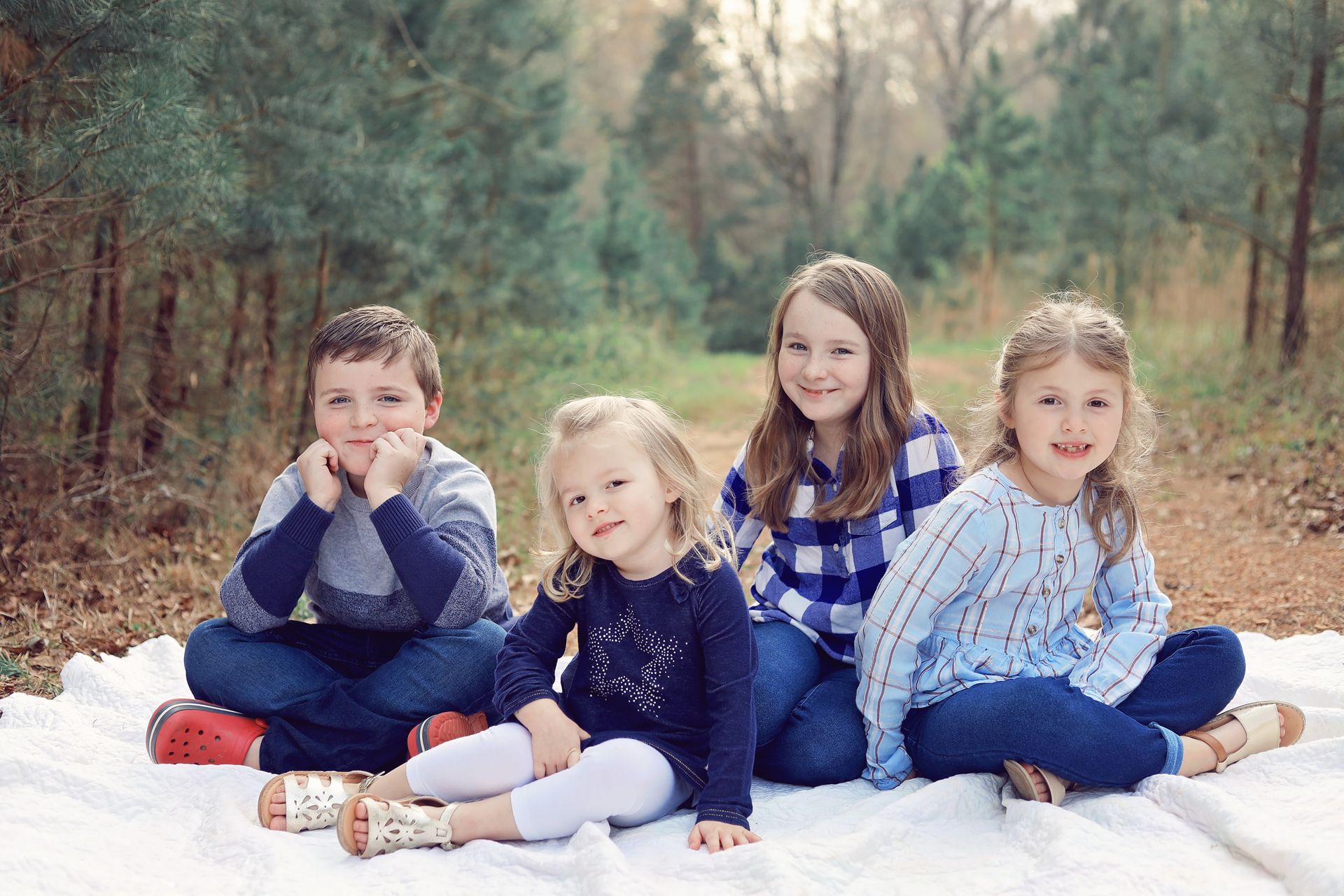 A group of children are sitting on a blanket in the woods.