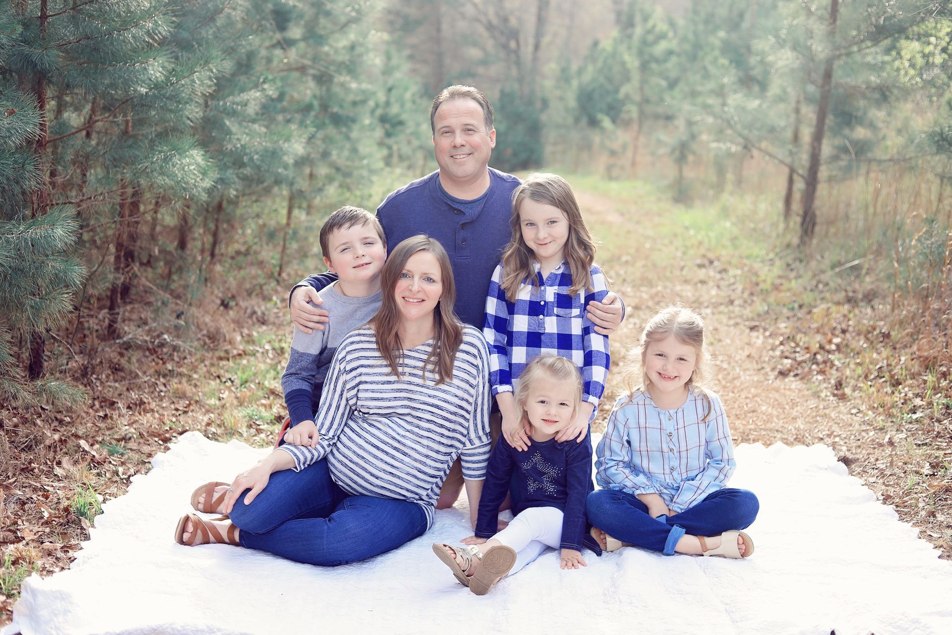 A family is posing for a picture while sitting on a blanket in the woods.