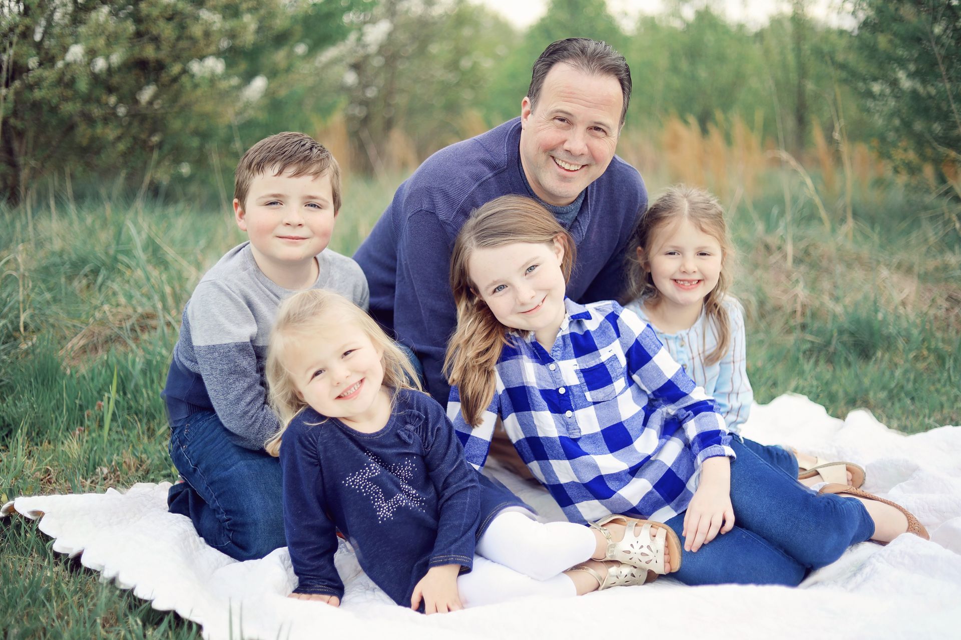 A man and three children are sitting on a blanket in the grass.
