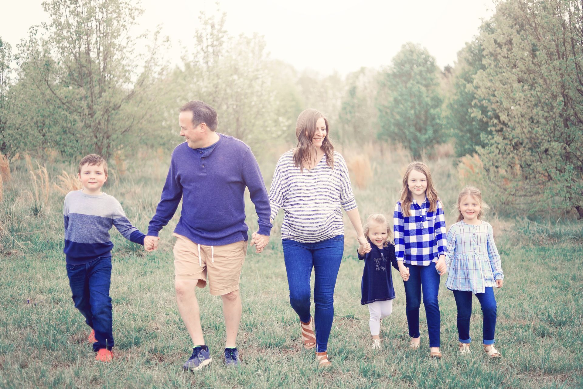 A family is walking through a field holding hands.