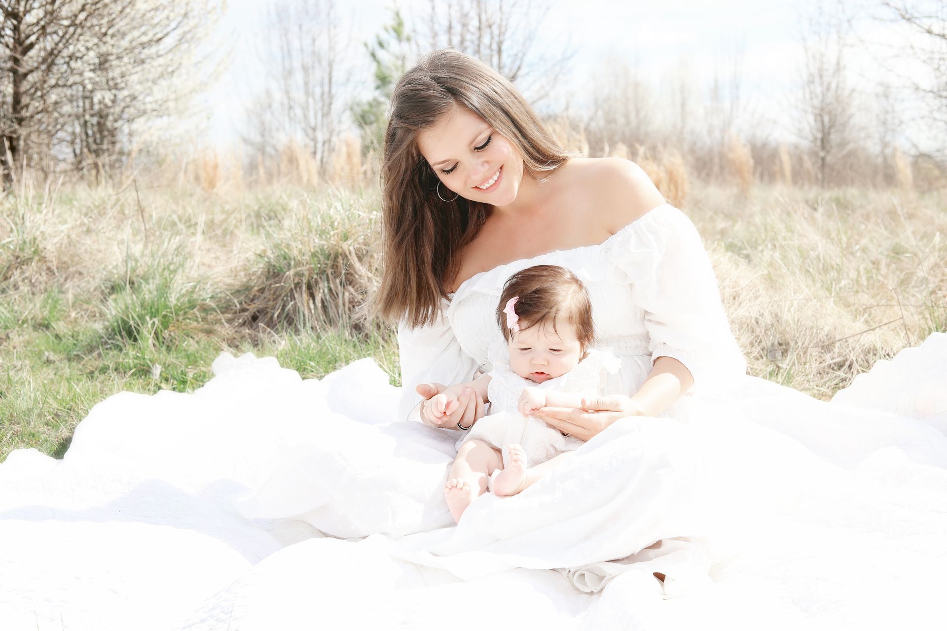 A woman in a white dress is holding a baby in a field.