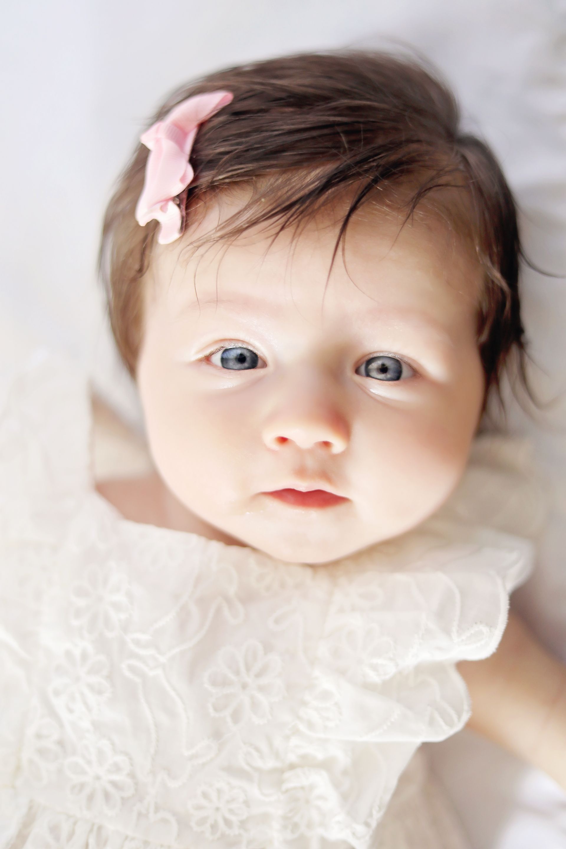 A baby girl with a pink bow in her hair is laying on a bed.