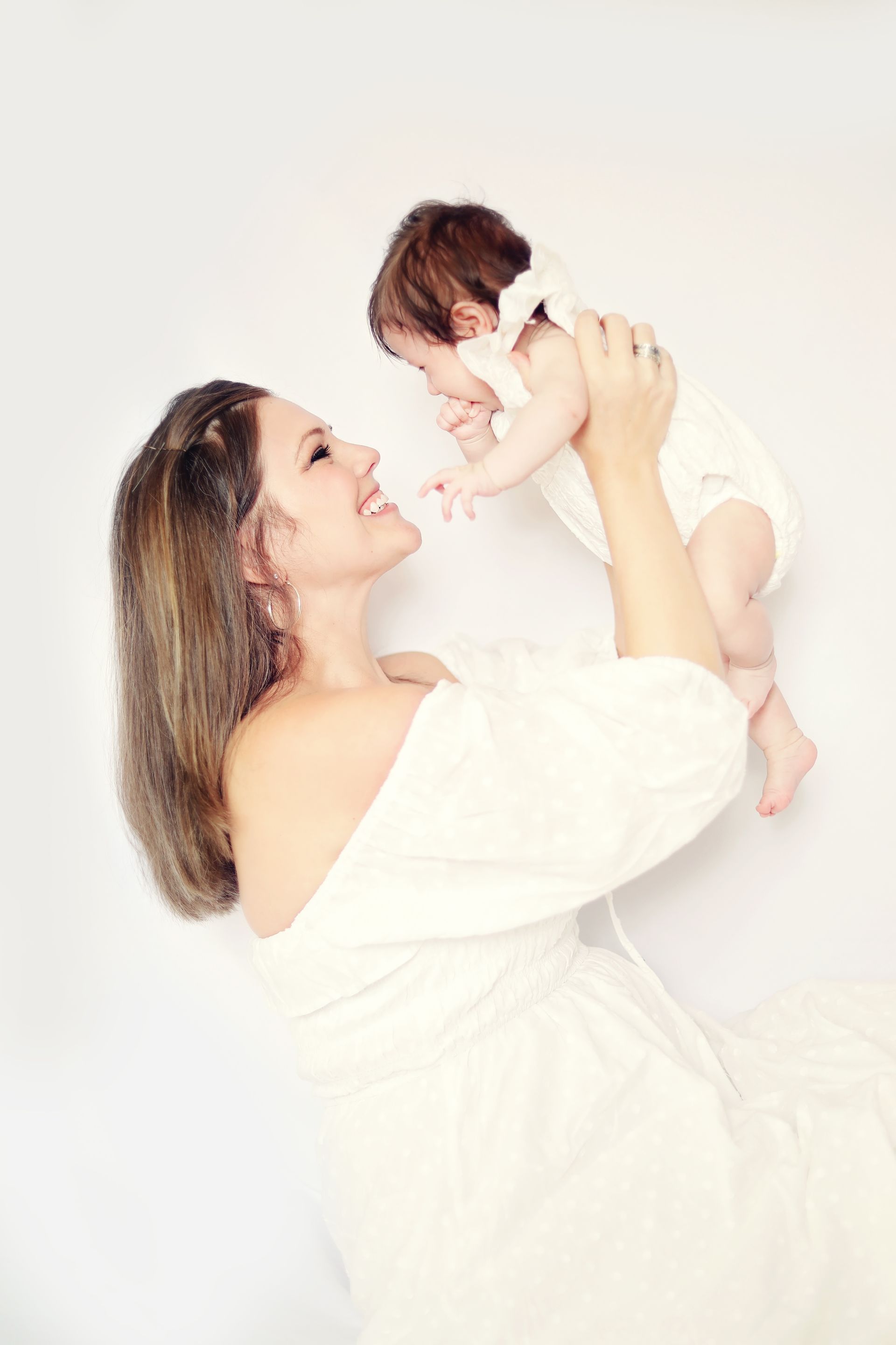 A woman in a white dress is holding a baby in her arms.