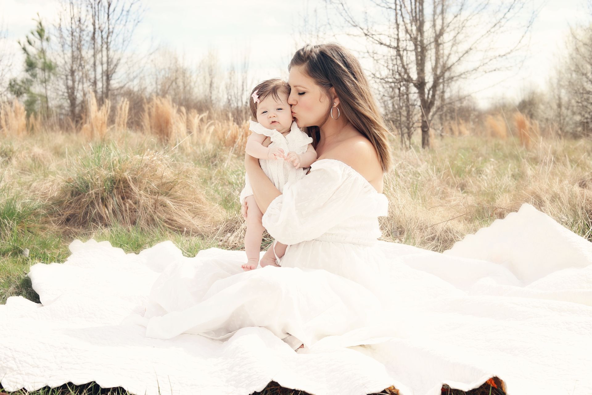 A woman in a white dress is holding a baby in a field.