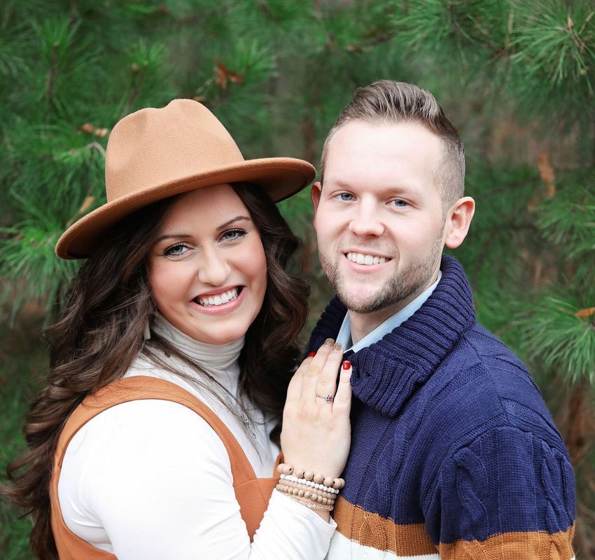 A man and a woman are posing for a picture and the woman is wearing a hat