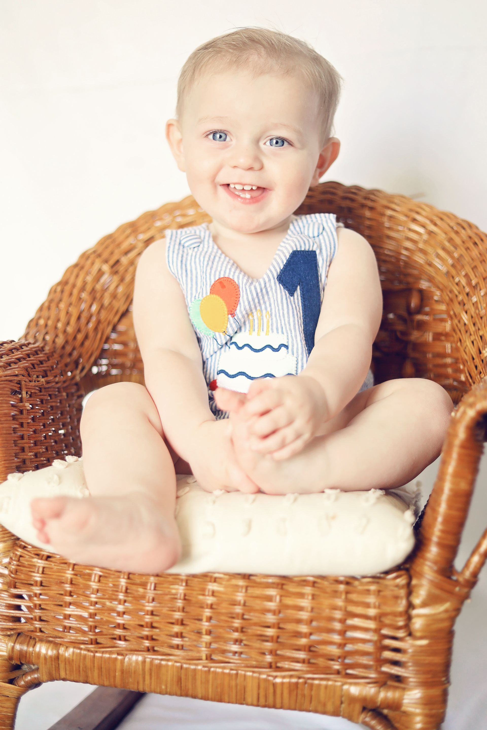A baby is sitting in a wicker chair and smiling.