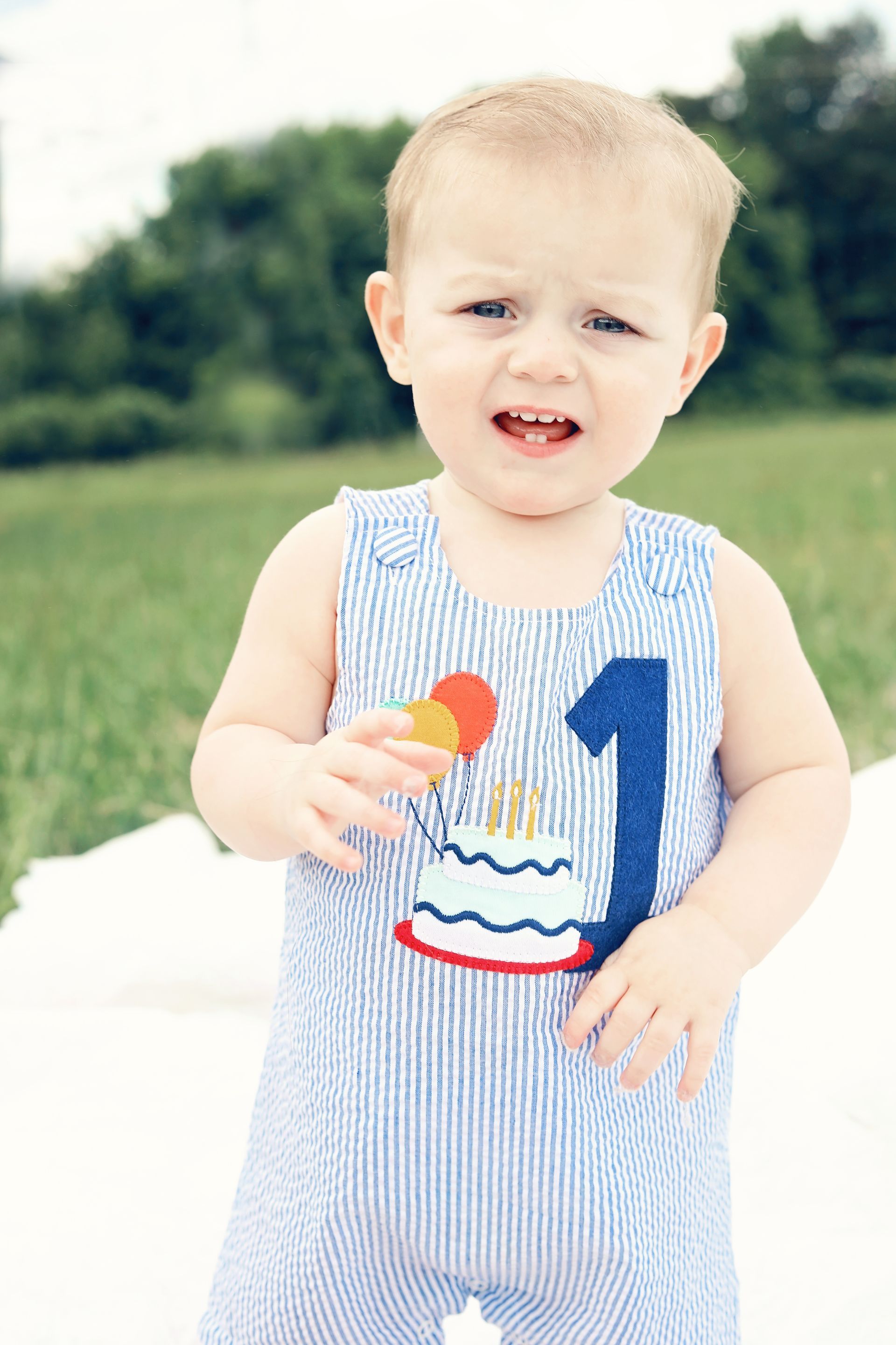A baby boy wearing a blue and white striped outfit is holding an ice cream cone.