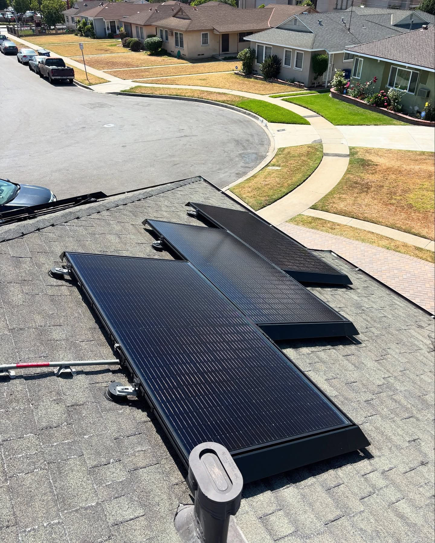 Solar panels on a rooftop with a suburban street and houses in the background. Sunny day.