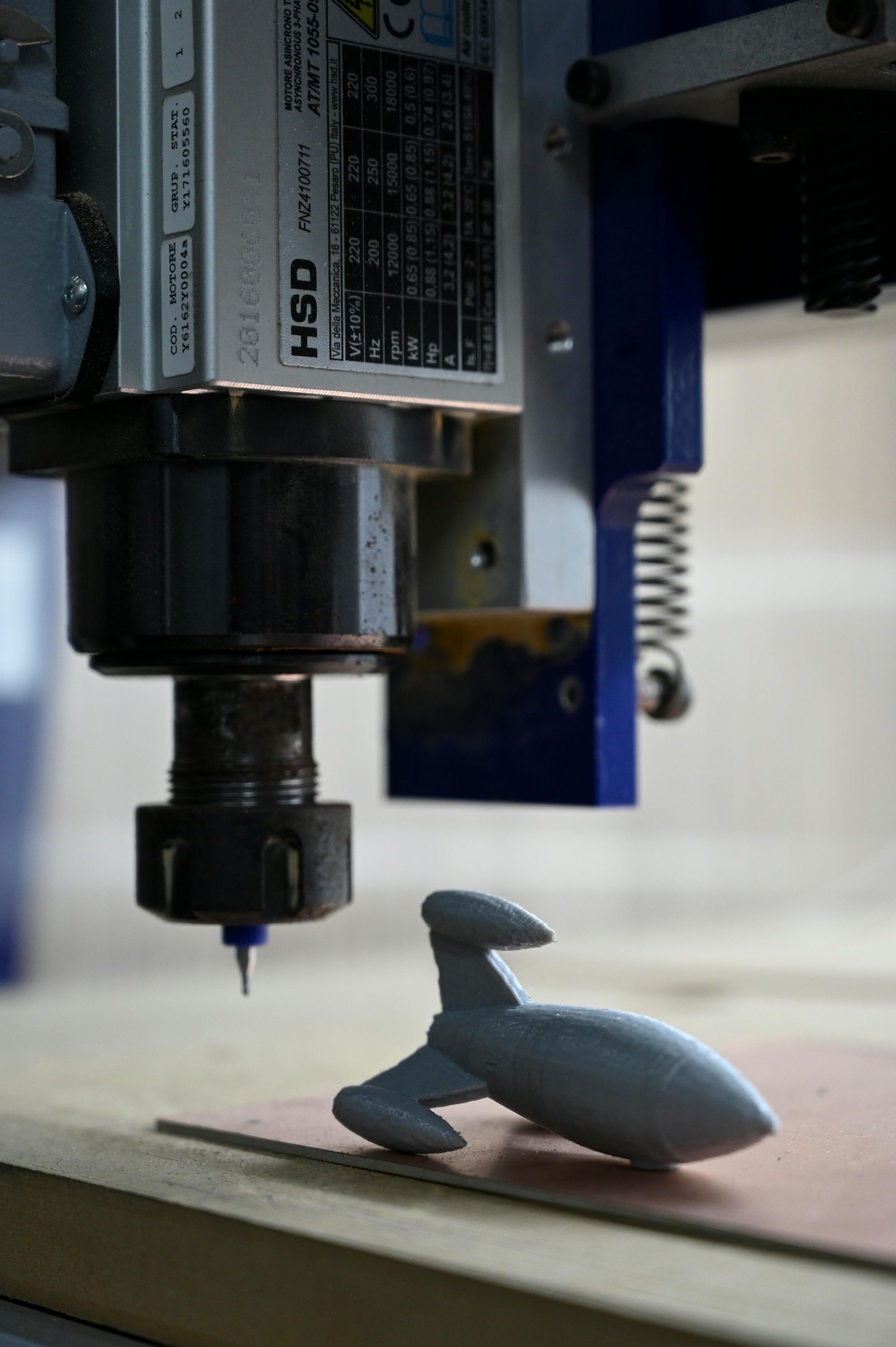 CNC machine with a blue and gray body carving a gray, toy rocket.