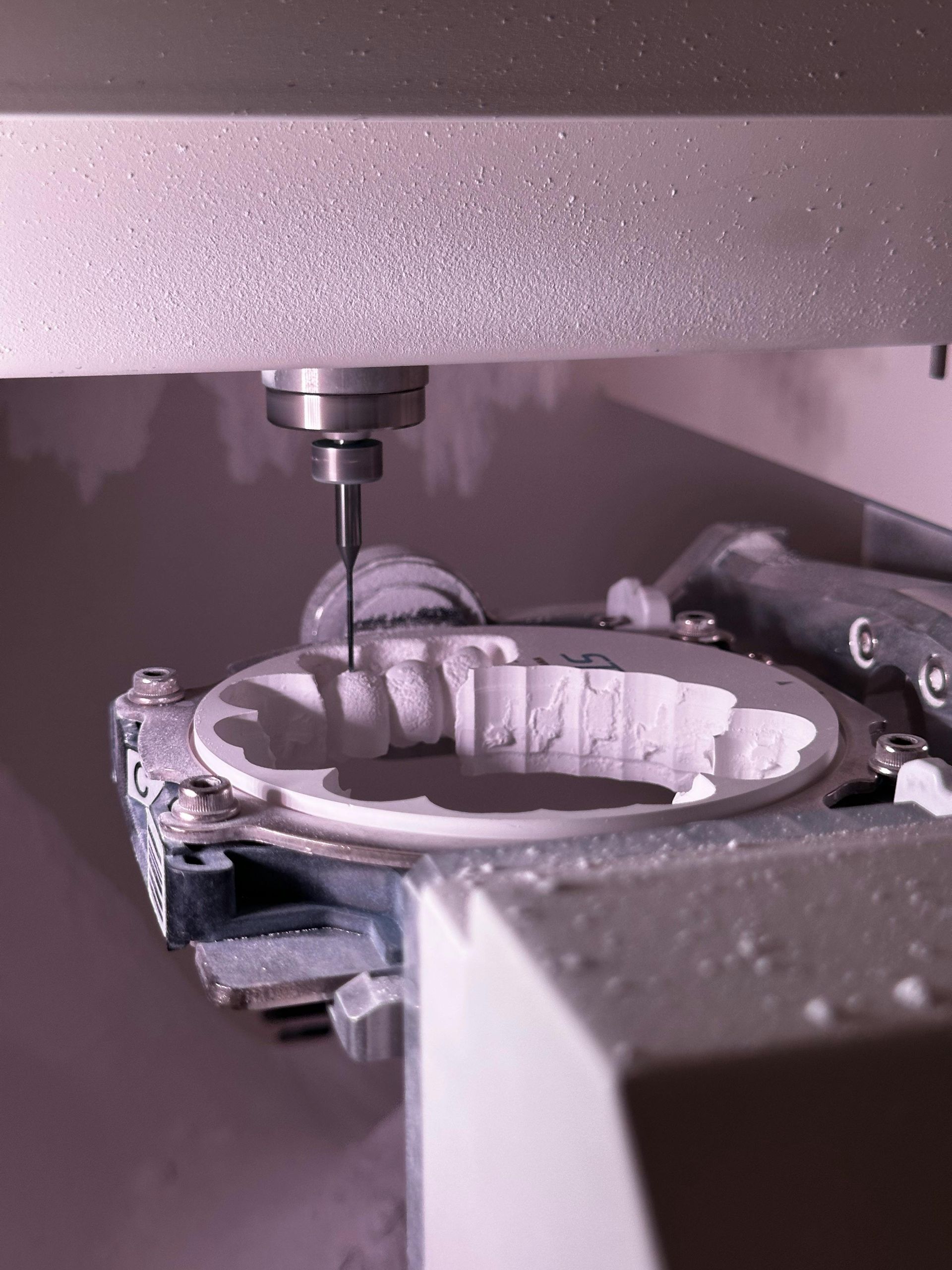 Dental milling machine cutting a white ceramic dental restoration.