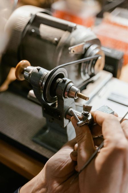 Hands using a jewelry lathe to shape a ring, workshop setting.
