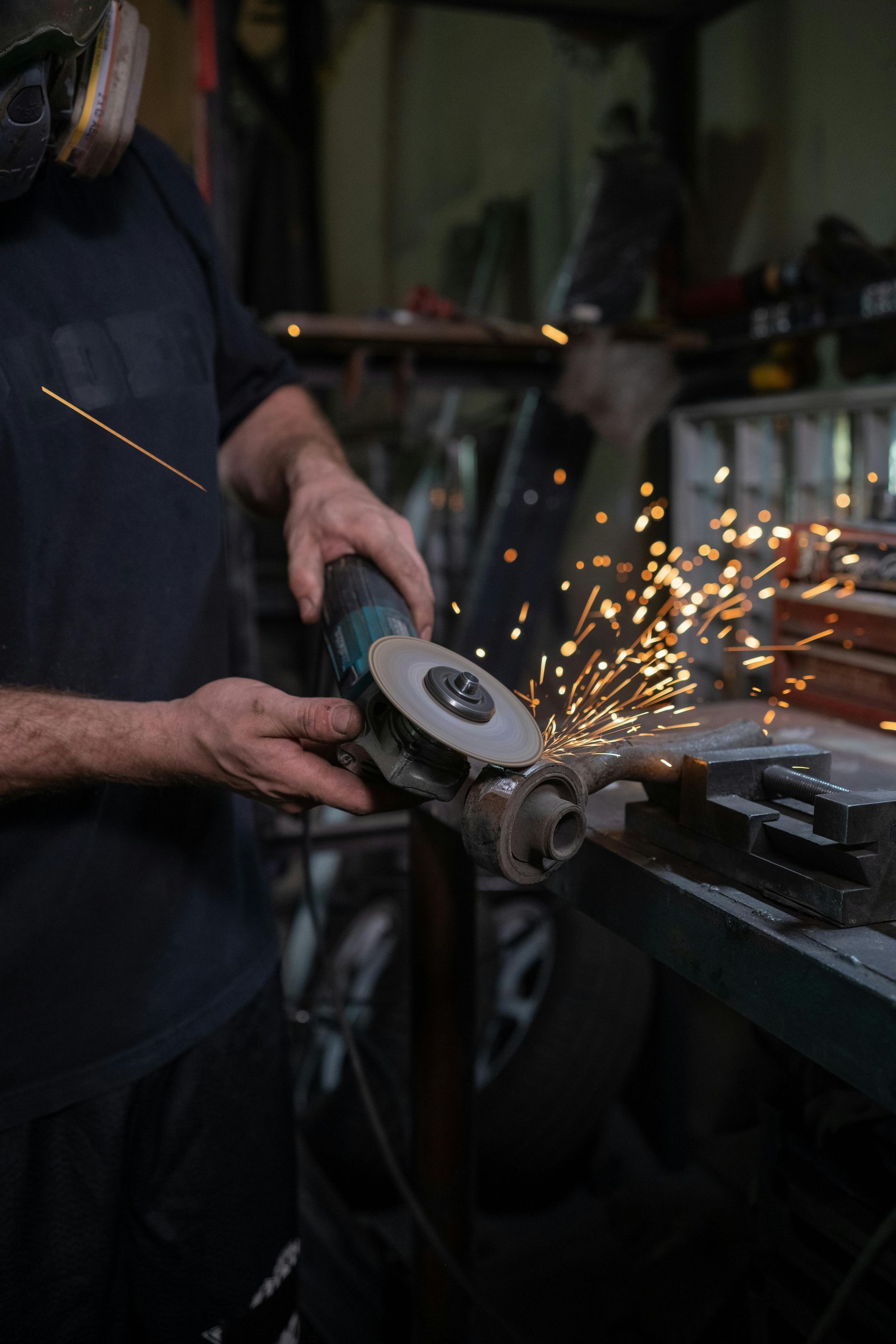 Person using an angle grinder, creating sparks. Workshop setting, dark clothing.