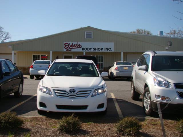 White car parked in front of Elder's Body Shop Inc. building with other cars.