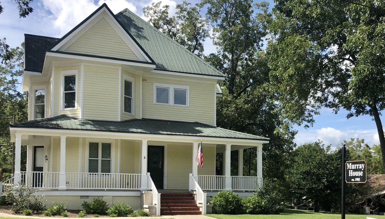 Yellow Victorian house with green roof and porch. 