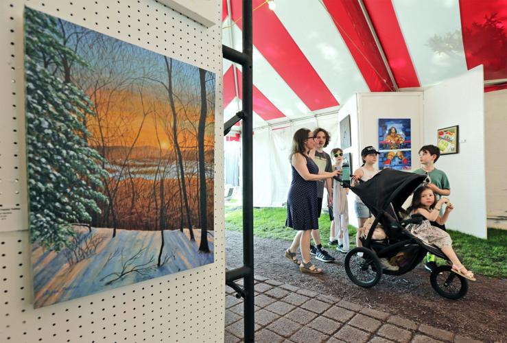 An art fair tent, a painting of a snowy landscape on display. People viewing paintings, one with a stroller.