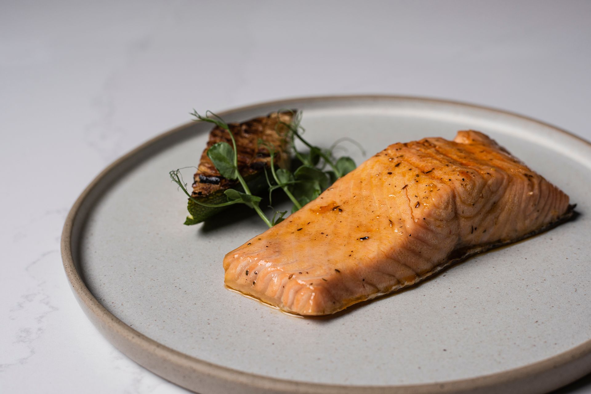 Pönnusteikt laxaflök á diski með grilluðu salati og grænu grænmeti.