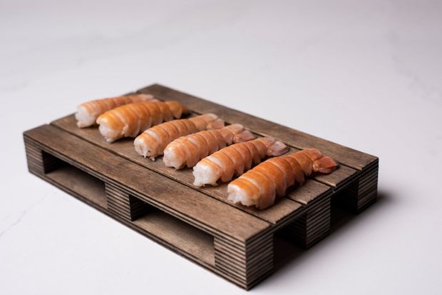 Sex eldaðir humarhalar raðaðir á lítinn trébretti á hvítum fleti.