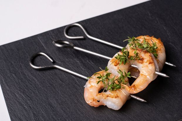 Rækjuspjót á svörtum leirplötum, skreytt með grænum kryddjurtum.