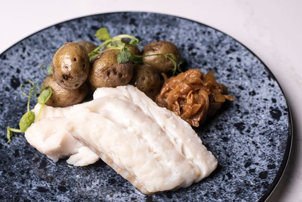 Diskur með fiski, kartöflum og lauk; eldaður réttur á bláum, flekkóttum diski.