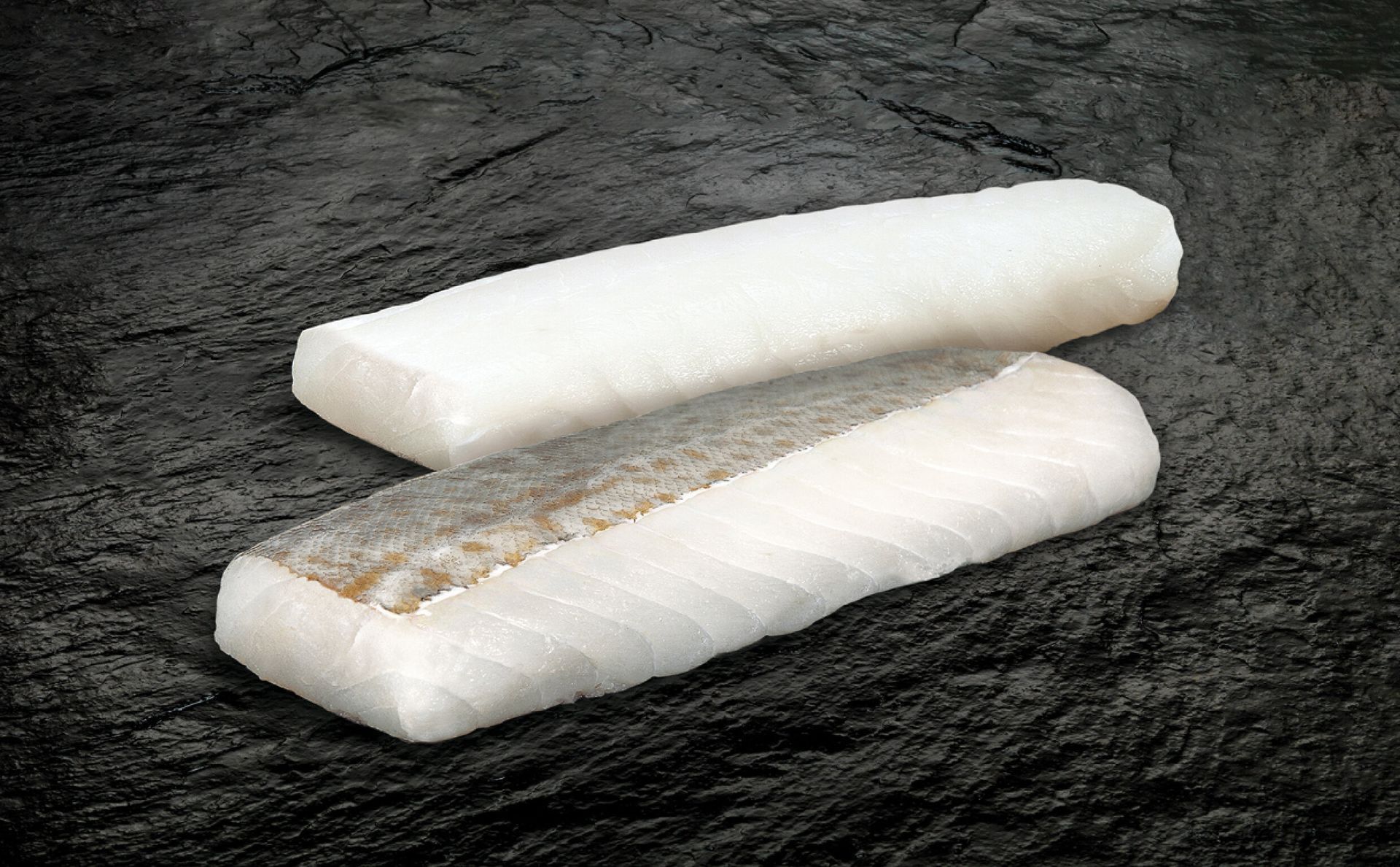 Tvö hvít fiskflök á dökkum áferðarflöt. Annað flökið er með gráa roð.