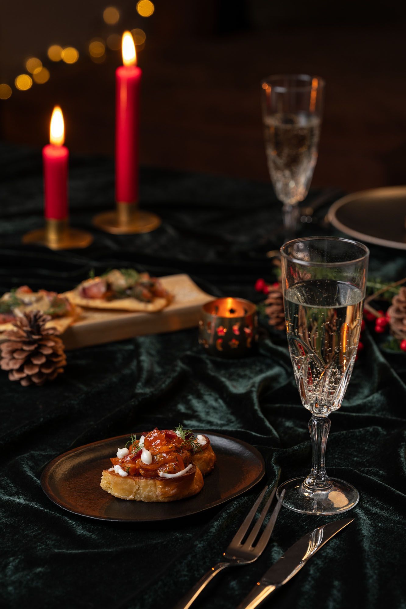 Nærmynd af hátíðarborði með forréttum, kampavíni, rauðum kertum og dökkgrænum dúk.