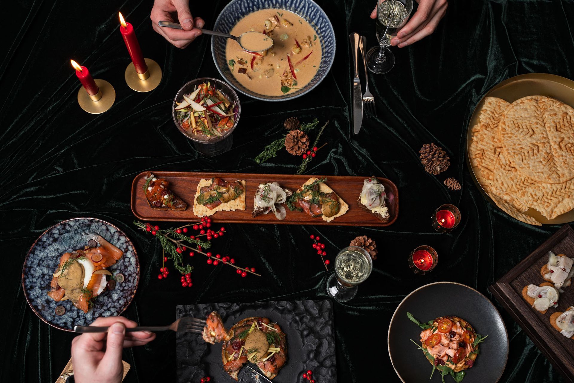 Sýn ofan frá af borðstofuborði með ýmsum réttum, tveimur einstaklingum sem njóta máltíðar og kveikt er á kertum.